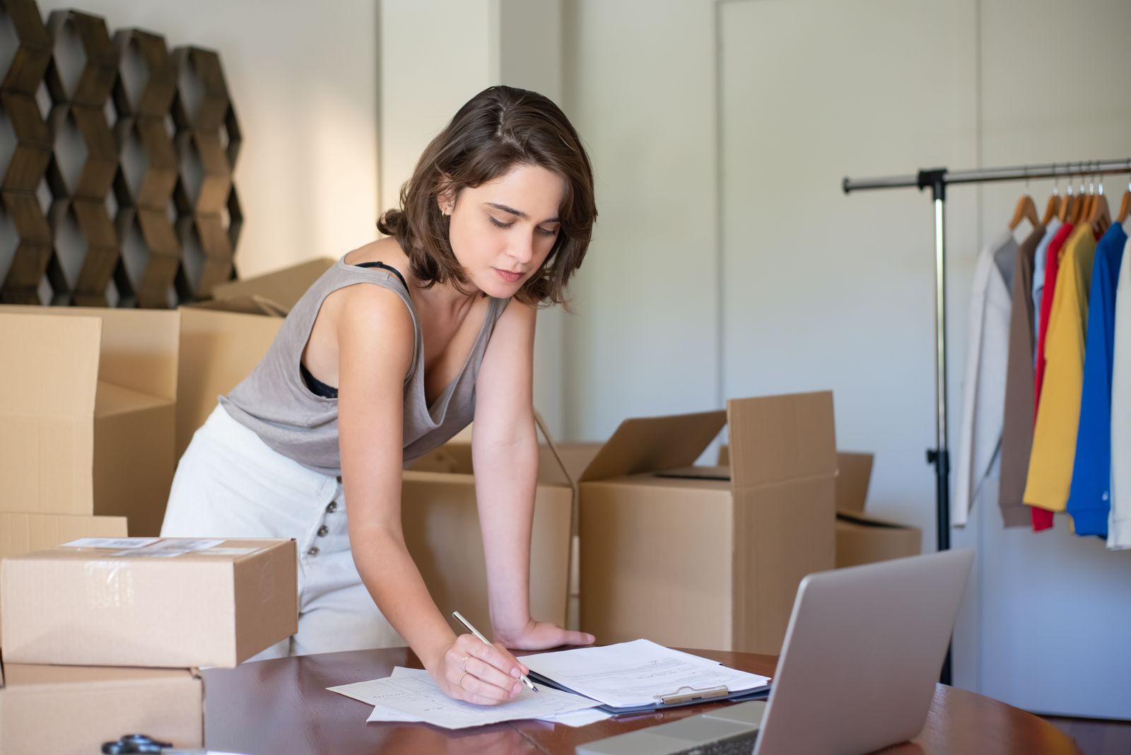 Small-business owner packing orders and filling out paperwork beside a laptop