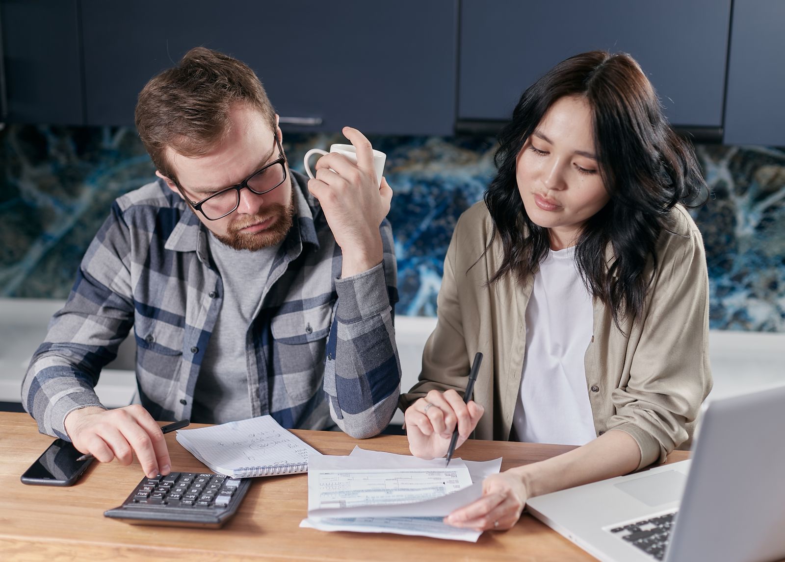 Couple reviewing household bills with a calculator and laptop at the kitchen table